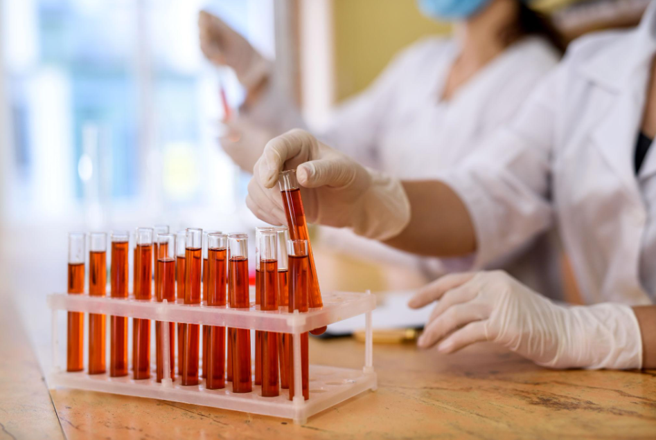 Lab technician in protective gear examining blood sample slides under microscope